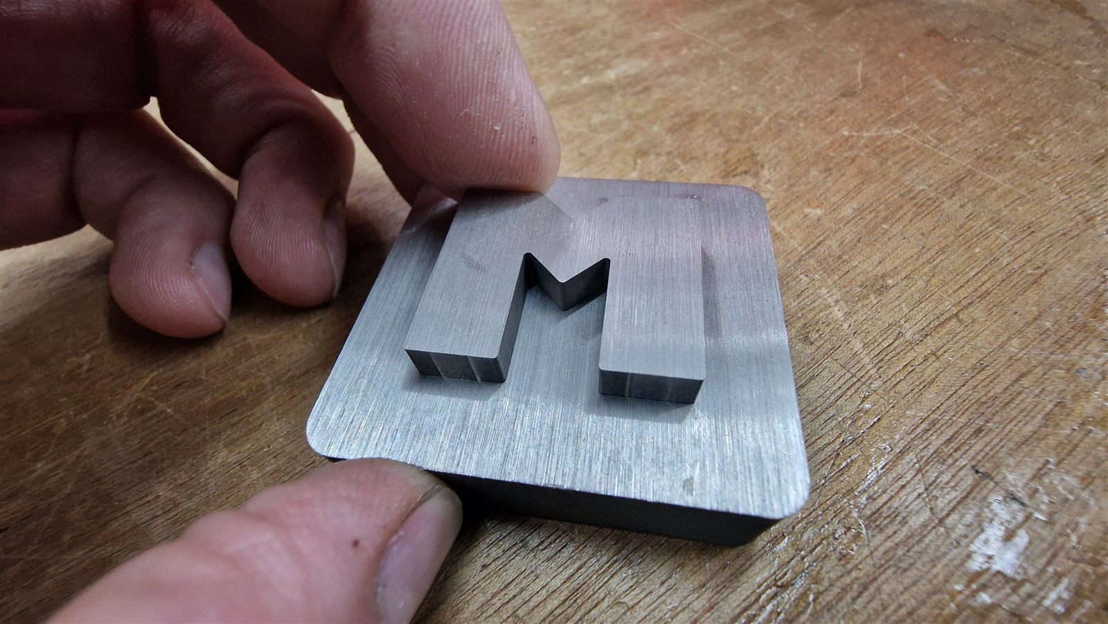 Letter M standing in a square plate