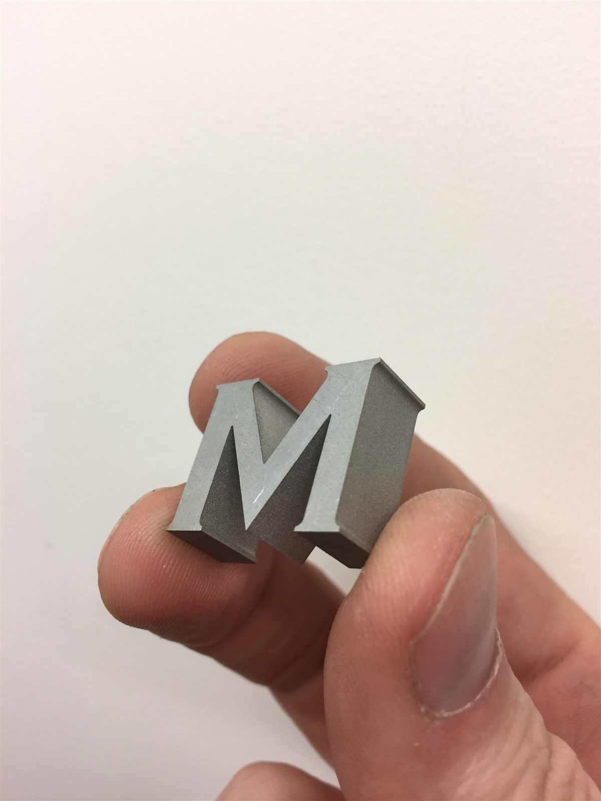Small metal letter M held in a hand